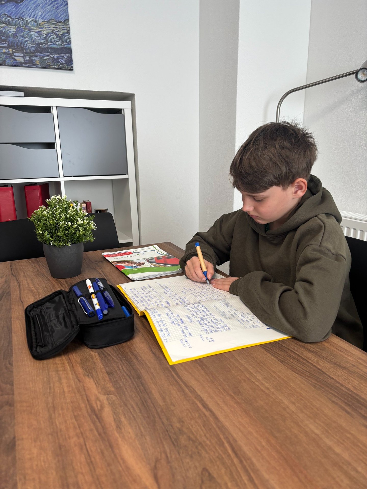 Schüler schreibt am Arbeitstisch in ein Heft, daneben liegt ein Englisch-Workbook